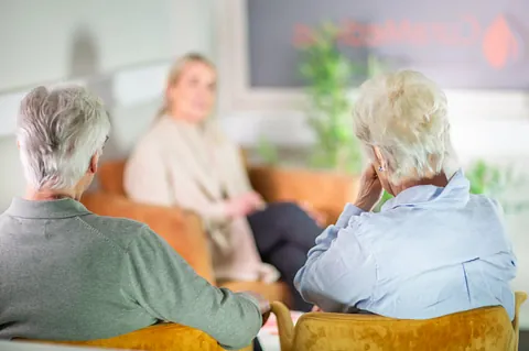 To eldre personer sittende i stol under samtale med terapeut